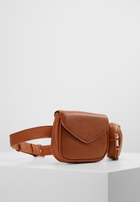 Ruskea nahkavyölaukku, jossa on suuri läppätasku ja pieni vetoketjullinen pyöreä pussi, esillä valkoisella pinnalla yksinkertaista taustaa vasten.