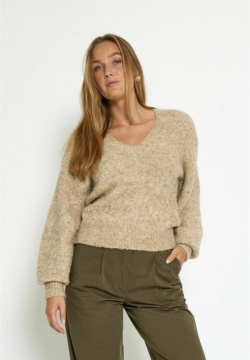 Beige V-hals trui met een zachte, gebreide textuur; heeft lange mouwen en een cropped, relaxte pasvorm. Combinatie met olijfgroene broek.