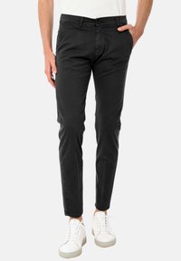Pantaloni slim-fit neri in cotone. Presentano una chiusura con zip, passanti per la cintura e due tasche davanti. Abbinati a sneakers bianche.