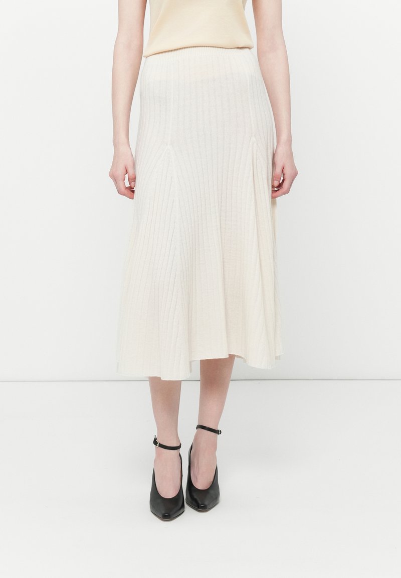 Cream ribbed knit midi skirt with a flared silhouette, featuring vertical lines and a wide waistband. Paired with black ankle-strap heels.