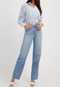  Lichtblauw button-up shirt met tekstuurstrepen, gecombineerd met hooggetailleerde, rechte jeans met vernietigde zomen en een lichte denimwas.