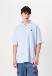 Gaiši zils polo krekls ar klasisku apkakli, īsām piedurknēm un mazu logotipus uz kreisā krūša. Izgatavots no mīksta kokvilnas auduma.