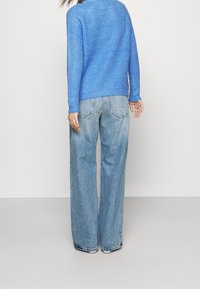 Pull bleu en tricot avec poignets et ourlet côtelés, associé à un jean denim bleu clair à jambes larges, doté de poches arrière et d'une finition délavée.