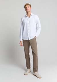 Witte button-up shirt met een puntige kraag, gecombineerd met slim-fit beige broek en lichte sneakers, met een gladde textuur en strakke lijnen.