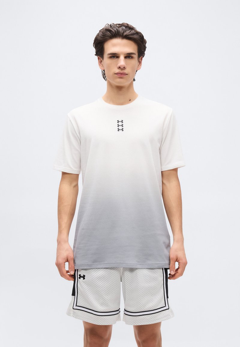 Νέος άνδρας που φορά ένα μπλουζάκι με διαβάθμιση από λευκό σε γκρι και λευκά αθλητικά σορτς από δίχτυ με μαύρο περίγραμμα, στέκεται μπροστά σε απλό λευκό φόντο.