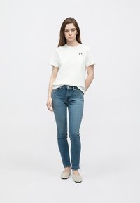 Biele bavlnené tričko s krátkym rukávom a okrúhlym výstrihom, zdobené malou grafikou. Kombinované s úzkymi modrými džínsami a svetlou obuvou.