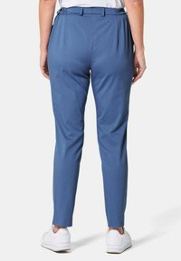 Pantalons bleus avec une texture lisse, une taille élastique et une coupe ajustée, associés à des baskets blanches. Aucun motif ni accent particulier.