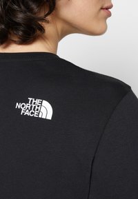 T-shirt en coton noir avec un logo blanc dans le haut du dos ; design classique à col rond avec des manches courtes et une texture lisse.