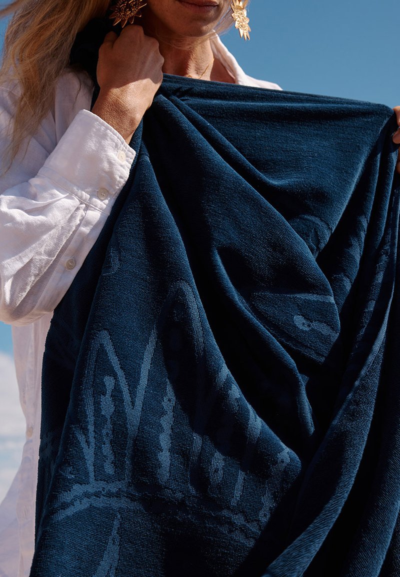 Couverture texturée bleu marine, présentant un subtil motif abstrait. Tissu doux drapé, mettant en valeur une riche couleur et des détails de design complexes.