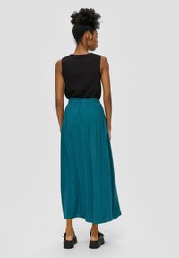 Teal maxi-rok met geplooid ontwerp, elastische tailleband en een gladde textuur, gecombineerd met een gestructureerde zwarte mouwloze top en chunky zwarte schoenen.