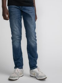 Jeans din denim albastru închis, cu croială slim, detalii subtile de uzură și un design clasic cu cinci buzunare. Asortate cu adidași deschiși.