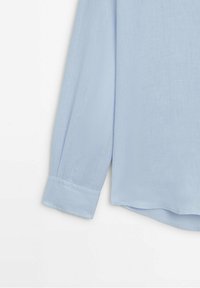 Camicia a maniche lunghe azzurro chiaro in un tessuto morbido e texturizzato. Presenta un colletto classico e polsini con bottoni, con un orlo leggermente curvo.