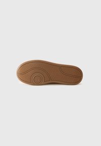 Suola di scarpa in gomma marrone con superficie testurizzata, caratterizzata da un dettaglio con logo circolare e linee di design distintive per la trazione.
