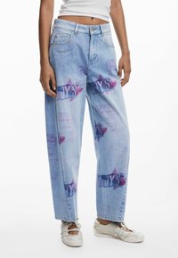 Jeans in denim azzurro chiaro con vestibilità ampia, caratterizzati da stampe grafiche multicolori, tra cui stelle e testo, sulla parte anteriore e sui lati.