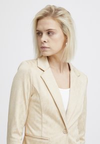 Béžový blazer so subtílnou zvieracou potlačou, s klopovým golierom, jedným gombíkom a dvoma prednými vreckami. Mäkký materiál s prispôsobeným strihom.