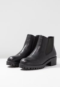 Mustat nilkkurit, joissa on sileä nahkapinta, joustavat sivupaneelit, pyöreä kärki ja paksupohjainen, kuvioitu pohja kohtuullisella korolla.