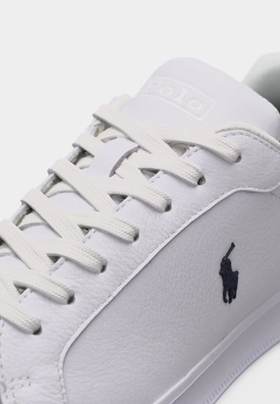 Κοντινό πλάνο ενός λευκού δερμάτινου αθλητικού παπουτσιού με λευκά κορδόνια και μαύρο κεντητό λογότυπο παίκτη πόλο στο πλάι.