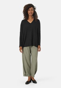Maglietta nera, larga, a maniche lunghe con scollo a V abbinata a pantaloni larghi verde chiaro e scarpe nere basse. Tessuti semplici in tutto.