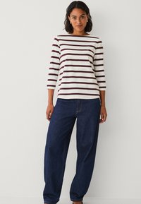 Gestreepte lange mouwen top in roomkleur met donker bordeauxrode strepen, gecombineerd met losse donkere spijkerbroek met een klassieke ronde halslijn.