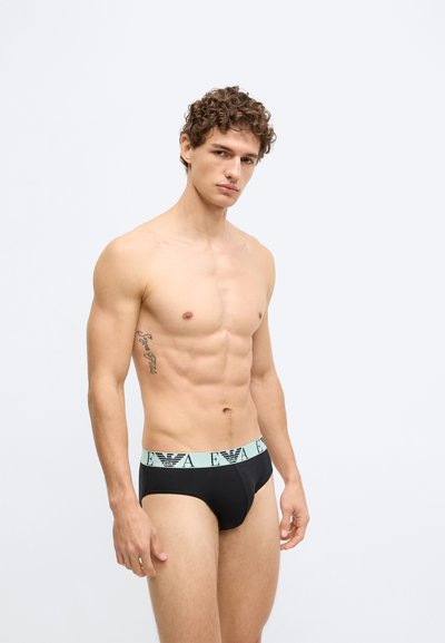 Cuecas pretas estilo slip com cós elástico azul claro com marca. Textura de tecido lisa e design ajustado.