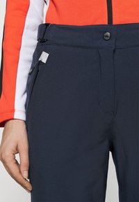 Pantaloni blu navy in tessuto liscio, con dettaglio tasca con cerniera, vita regolabile e chiusura frontale con bottone.
