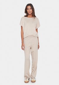 Beiges gestricktes Loungewear-Set mit einem lockeren kurzen Ärmel-Shirt und weiten Hosen mit elastischem Bund, kombiniert mit hellen Sneakers.