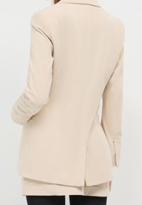 Beżowa marynarka z sztruksu o dopasowanym kroju, z klapami z wycięciem i rozcięciem z tyłu, z długimi rękawami i gładkim, teksturowanym wykończeniem.