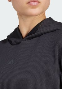 Sweat à capuche noir avec motif texturé, arborant un logo discret dans le coin supérieur gauche. Le tissu semble léger et respirant.