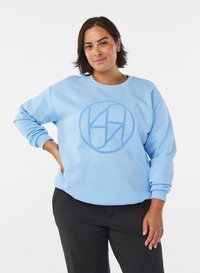 Light blue sweatshirt with a crew neck, ribbed cuffs, and an embroidered circular logo in a slightly darker blue. Smooth texture, relaxed fit.
