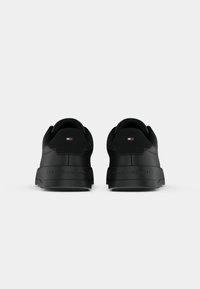 Pereche de pantofi sport negri, tip low-top, cu un logo embosat și un mic logo în roșu, alb și albastru pe tab-ul călcâiului, prezentate din spate.