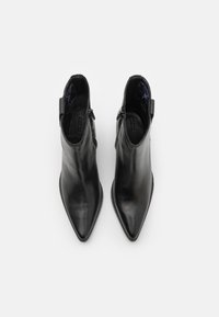 Bottes noires en cuir à la cheville avec un bout pointu, dotées d'une fermeture éclair sur le côté et d'un petit talon. L'intérieur est doublé d'un tissu doux.