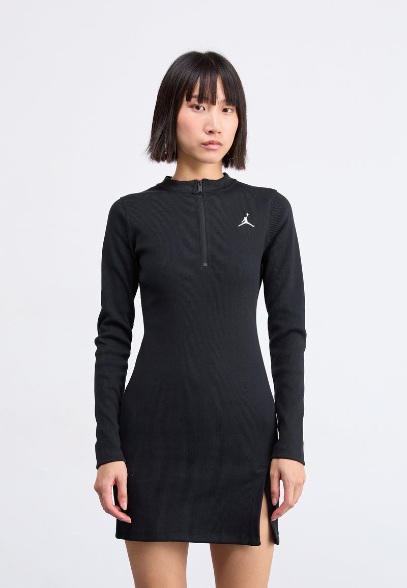 Abito nero a maniche lunghe con un design aderente, tessuto a coste testurizzato, colletto con zip a un quarto e dettaglio con spacco laterale. Presenta un logo bianco.