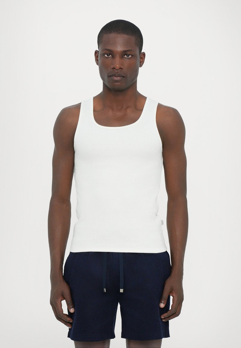 White ribbed tank top, sleeveless, with a rounded neckline. Paired with navy blue textured shorts featuring an elastic waistband and drawstring.