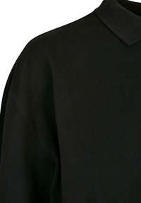 Svart polo skjorte med teksturert stoff. Har klassisk krage og avslappet passform, med synlige sømdetaljer på skuldrene.