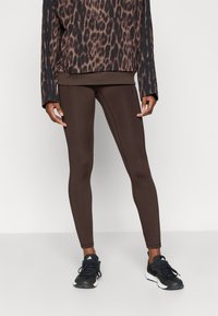 Hnedé legíny s priliehavým strihom, v kombinácii s čierno-hnedým dlhým rukávom s leopardím vzorom. Topánky sú čierne s bielymi detailmi.