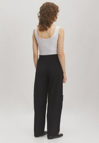 Schwarze weit geschnittene Cargo-Hosen mit Seitentaschen, aus einem glatten Stoff gefertigt. Getragen mit einem enganliegenden weißen Tanktop, das ein einfaches Design zeigt.