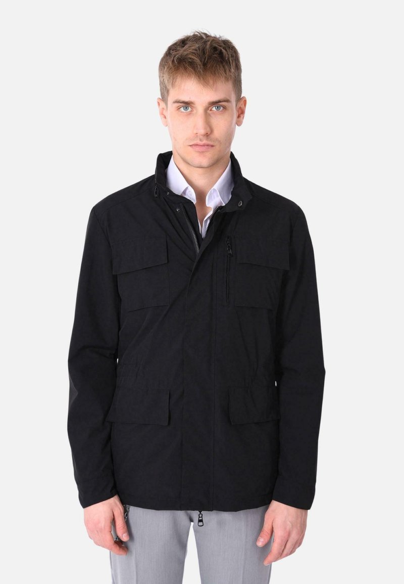 Giacca nera in tessuto con colletto alto, zip frontale e diverse tasche. Presenta un design strutturato e una vestibilità su misura.