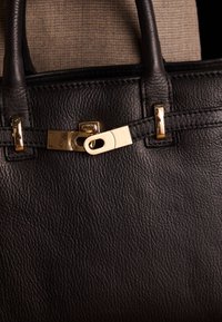 Borsa a mano in pelle nera con superficie testurizzata, caratterizzata da hardware dorato e un'unica chiusura a scatto. Design strutturato con manici robusti.