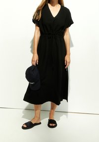 Czarna sukienka do kolan z dekoltem w kształcie litery V i krótkimi rękawami. Posiada regulowany sznurek w pasie. Zestawiona z czarnymi klapkami i granatową czapką.