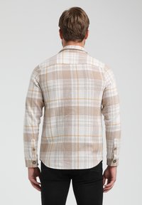 Camicia di flanella a quadri beige con accenti bianchi e gialli, polsini con bottoni e orlo curvo, vista dalla schiena.