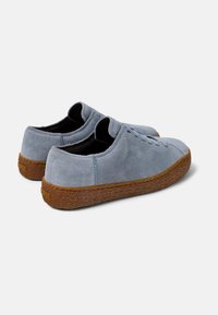 Scarpe basse in suede di colore azzurro chiaro con suole in gomma marrone testurizzata. Presentano punte arrotondate e un design con lacci. Fodera interna nera.