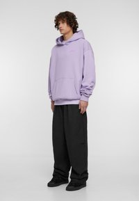 Lavanda kapuca s kengursko žepom i kapuljačom na uzicu, uparena s crnim širokim hlačama i crnim tenisicama. Jednostavan dizajn, meka tekstura.