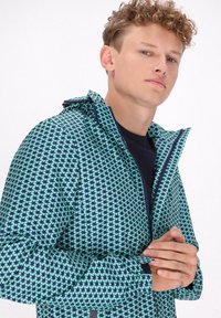 Jachetă cu un model verde și bleumarin, cu glugă, având un design geometric în formă de stea, închidere cu fermoar și manșete ajustabile. Țesătura pare netedă.