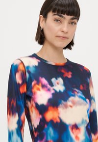 Blusa de manga longa em tecido elástico com um padrão floral multicolorido sobre um fundo escuro. Possui um decote redondo e costuras em contraste.