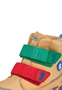 Chaussure enfant couleur fauve avec des bandes velcro vertes et rouges illustrées de petits singes et un logo bleu sur le côté.