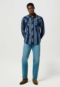 Marineblå langærmet skjorte med lyseblåt stribet mønster; to forlommer. Kombineret med lyseblå jeans og brune cowboystøvler.
