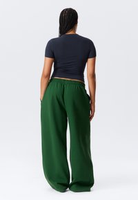 Tamsiai mėlynas trumpas marškinėlis su trumpomis rankovėmis derinamas su laisvomis žaliomis laisvalaikio kelnėmis, turinčiomis elastinę juosmenį ir šonines kišenes.