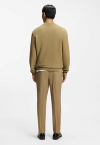 Maglione color cammello con trama a coste e vestibilità rilassata abbinato a pantaloni color cammello coordinati. L'outfit presenta un design semplice senza motivi visibili.