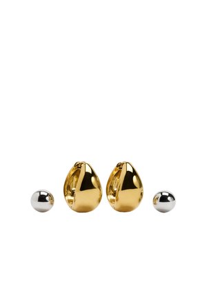 Kolczyki z metalu w kolorze złota w kształcie kropli, z polerowaną, refleksyjną powierzchnią, obok małej, srebrnej kulki.