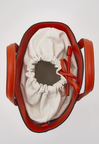 Sac à main en cuir orange avec de larges anses et une pochette en tissu blanc à cordon à l'intérieur, vu de dessus.
